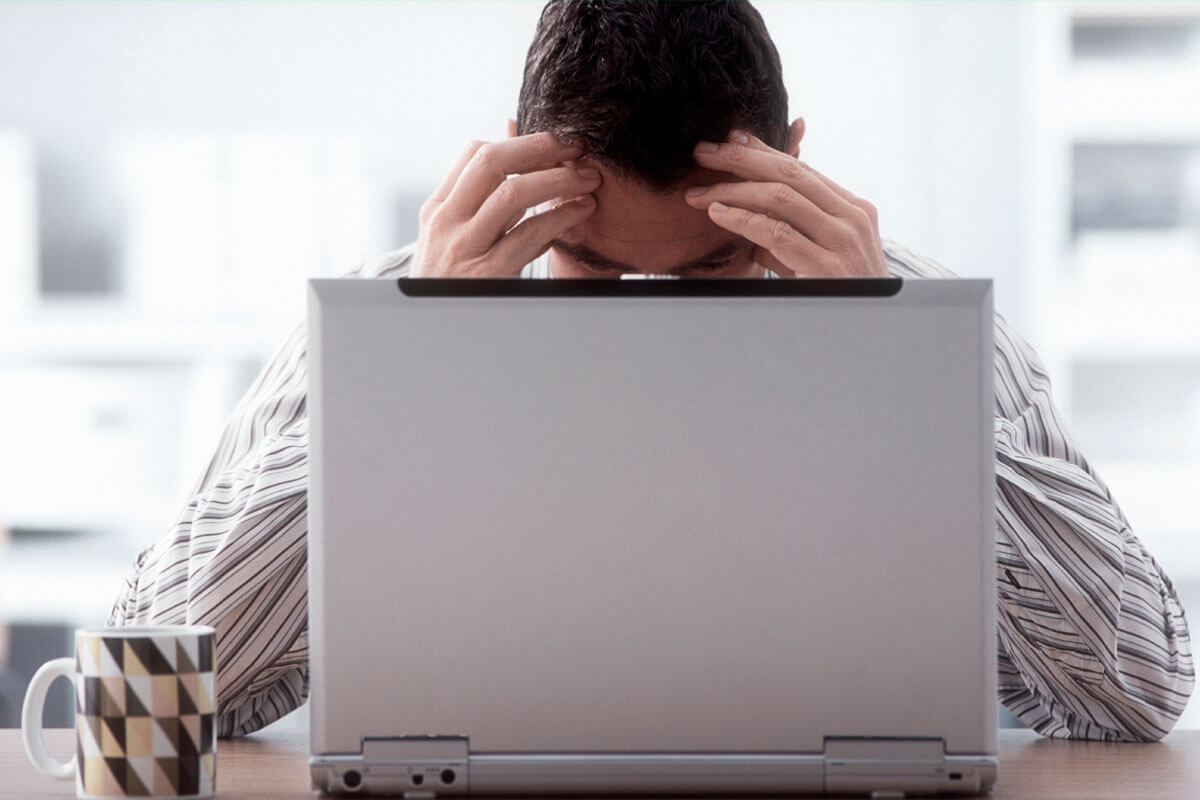 Mann mit Konzentrationsproblemen hinter dem Laptop. Dem kann auch ein Vitaminmangel zugrunde liegen.