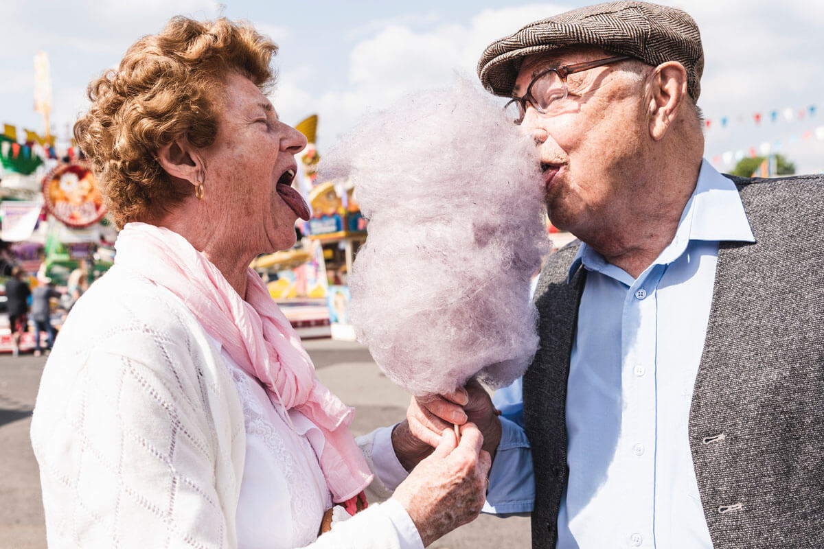 
Ein altes Ehepaar isst auf der Kirmes fröhlich zusammen rosa Zuckerwatte. 