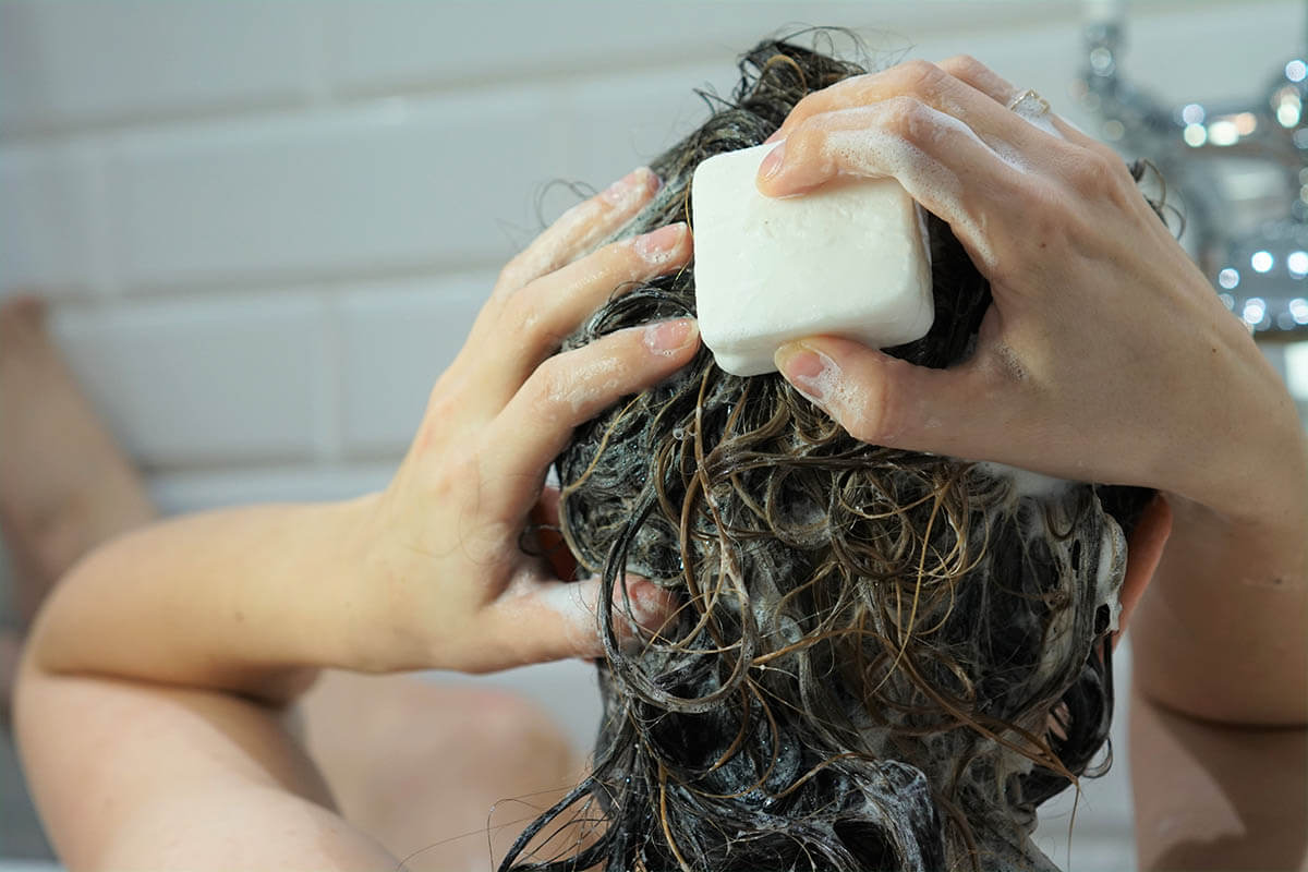 Frau seift sich die Haare mit festem Shampoo ein. Festes Shampoo spart Verpackungsmüll.